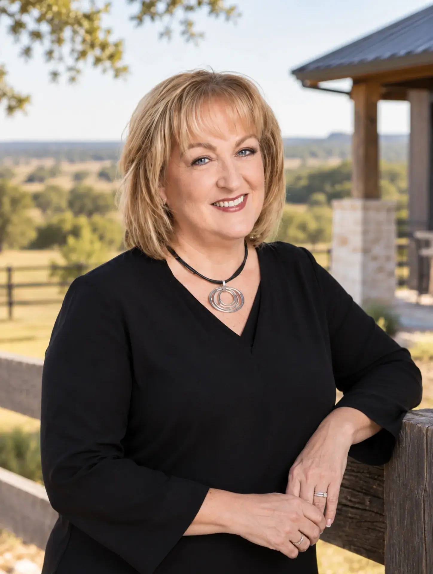Blond Woman in a black dress in front of a ranch fence